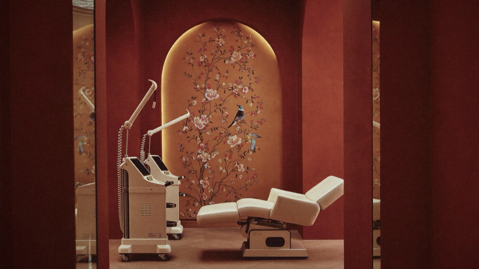 A treatment room with a cream treatment chair and two laser devices in front of a backlit arched mural of blossom and birds.